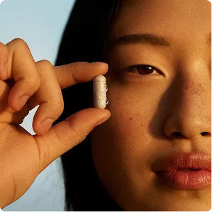 A woman holding a Kētos capsule beside her face in golden-hour light