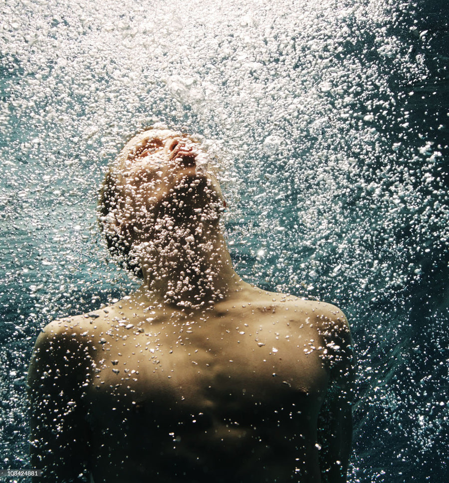 A man underwater, face raised, surrounded by bubbles