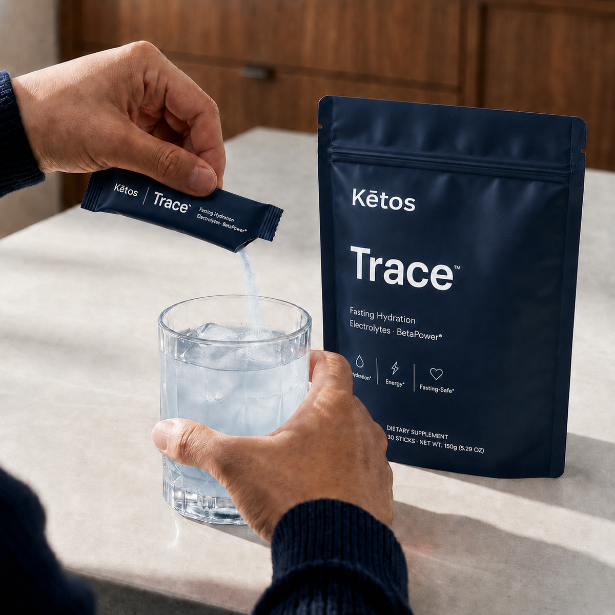A Trace electrolyte stick pouring into a glass of ice water beside the Kētos Trace pouch